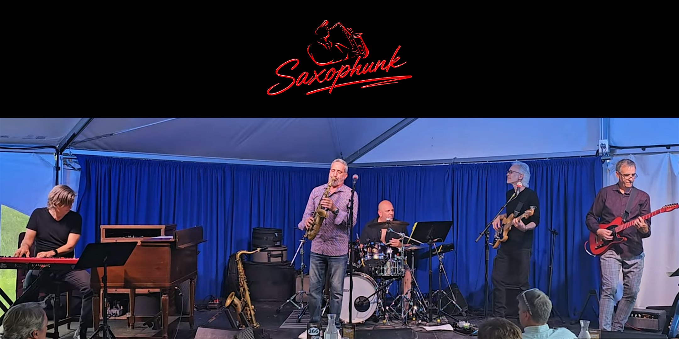 Live jazz band Saxophunk performing on a blue-curtained stage under a tent; keyboardist left, saxophonist center, drummer, bassist, and guitarist playing.