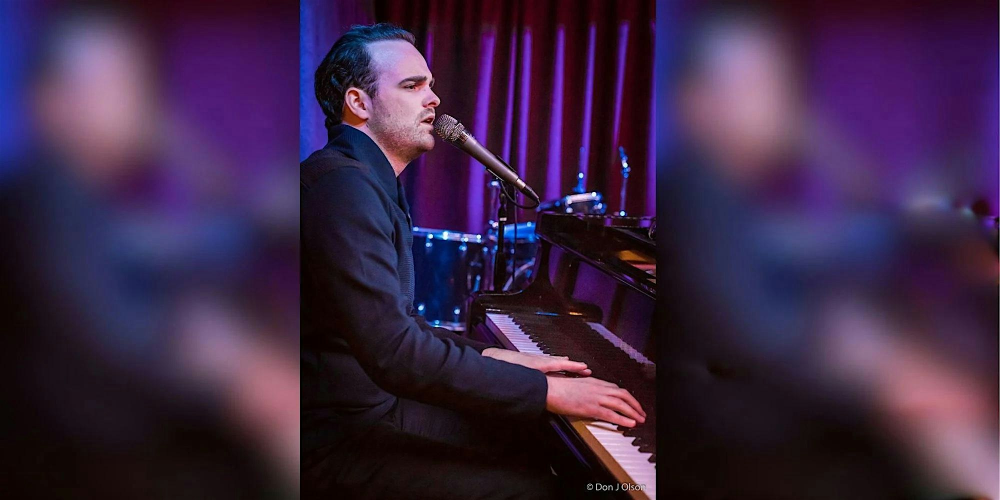 Male pianist singing into a microphone while playing a grand piano on a purple-lit stage with drums in the background