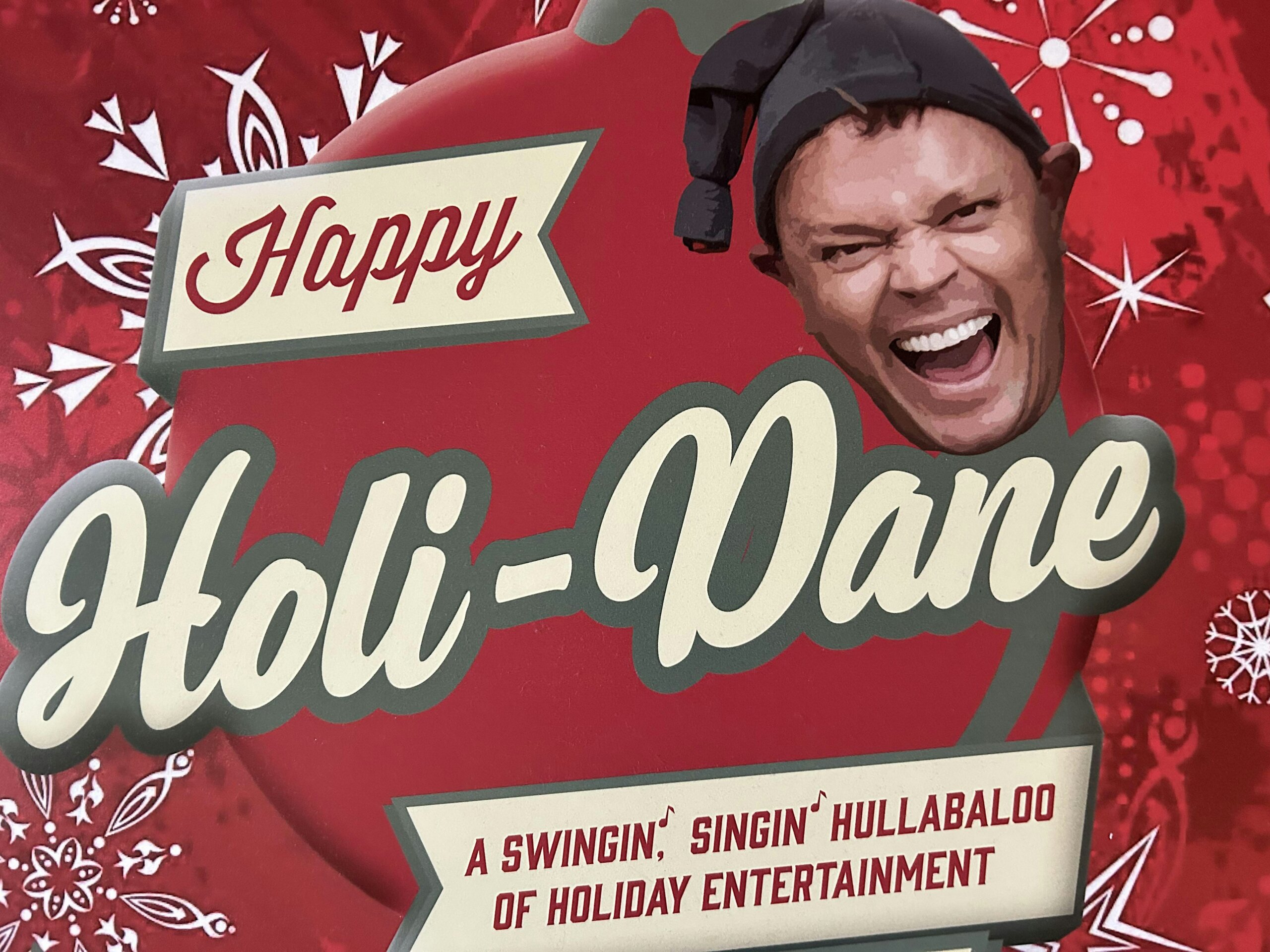 Promotional holiday poster with a smiling man in a hat, a 'Happy' banner, and bold script text advertising a swingin' holiday entertainment show.