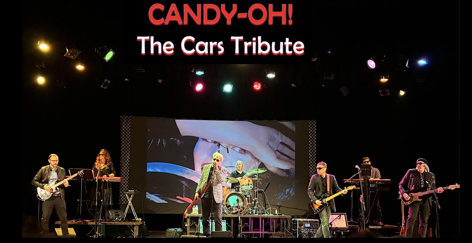 Candy-OH! Cars Tribute band performing on a lit stage with a large banner above and a video screen backdrop.