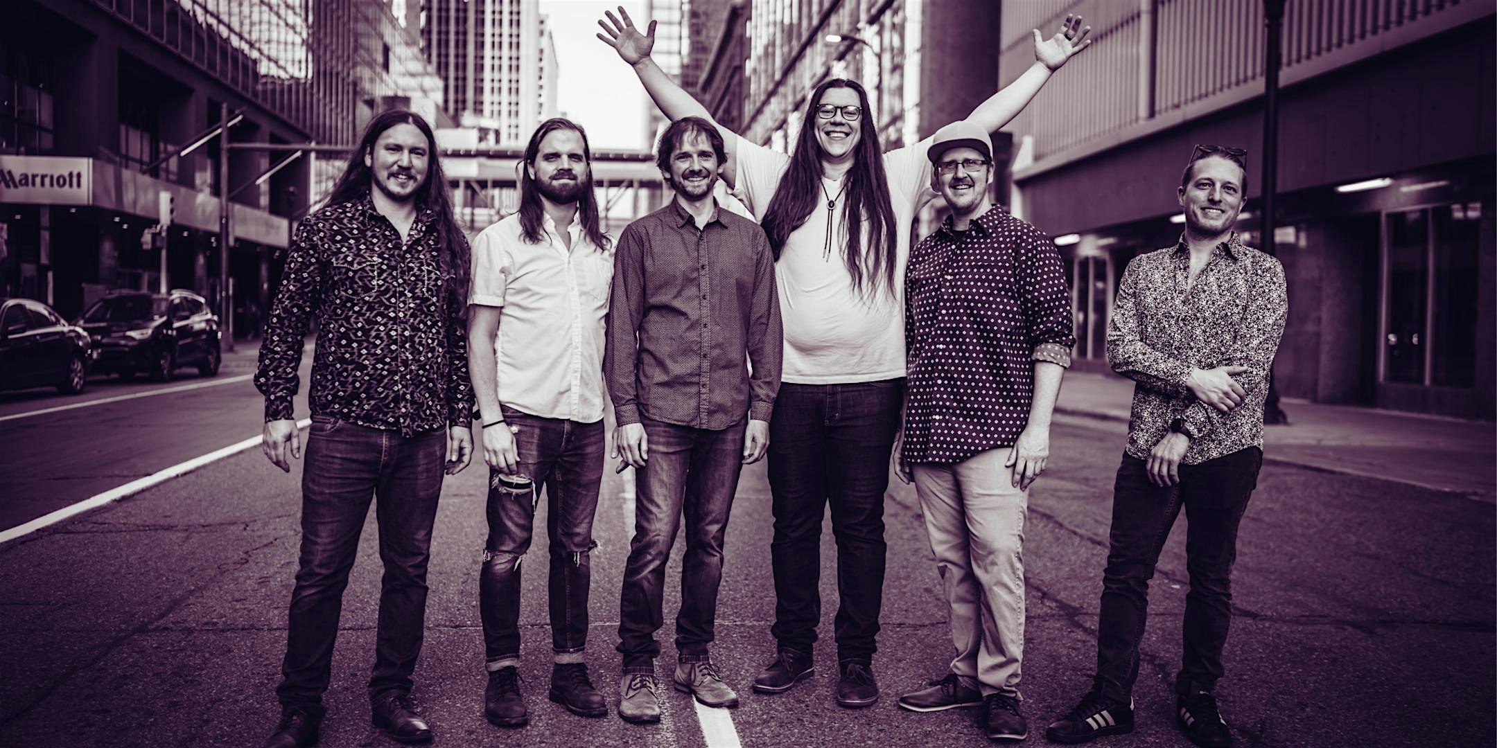 Six friends standing in the middle of a city street, smiling at the camera.